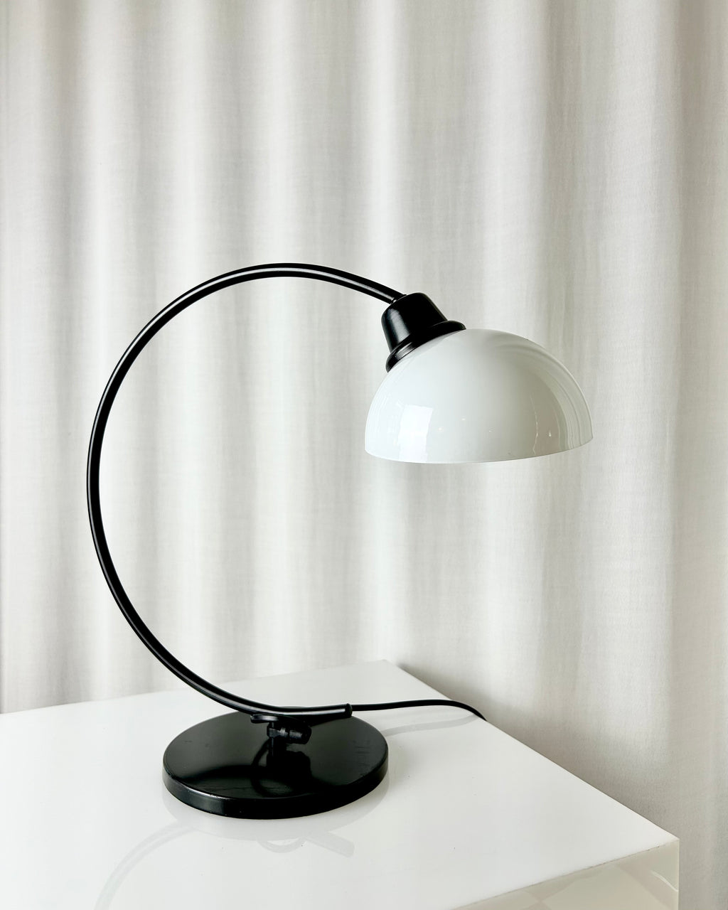 Vintage IKEA Harmoni table lamp featuring a black arched metal frame and a white glass shade, 1980s postmodern design.
