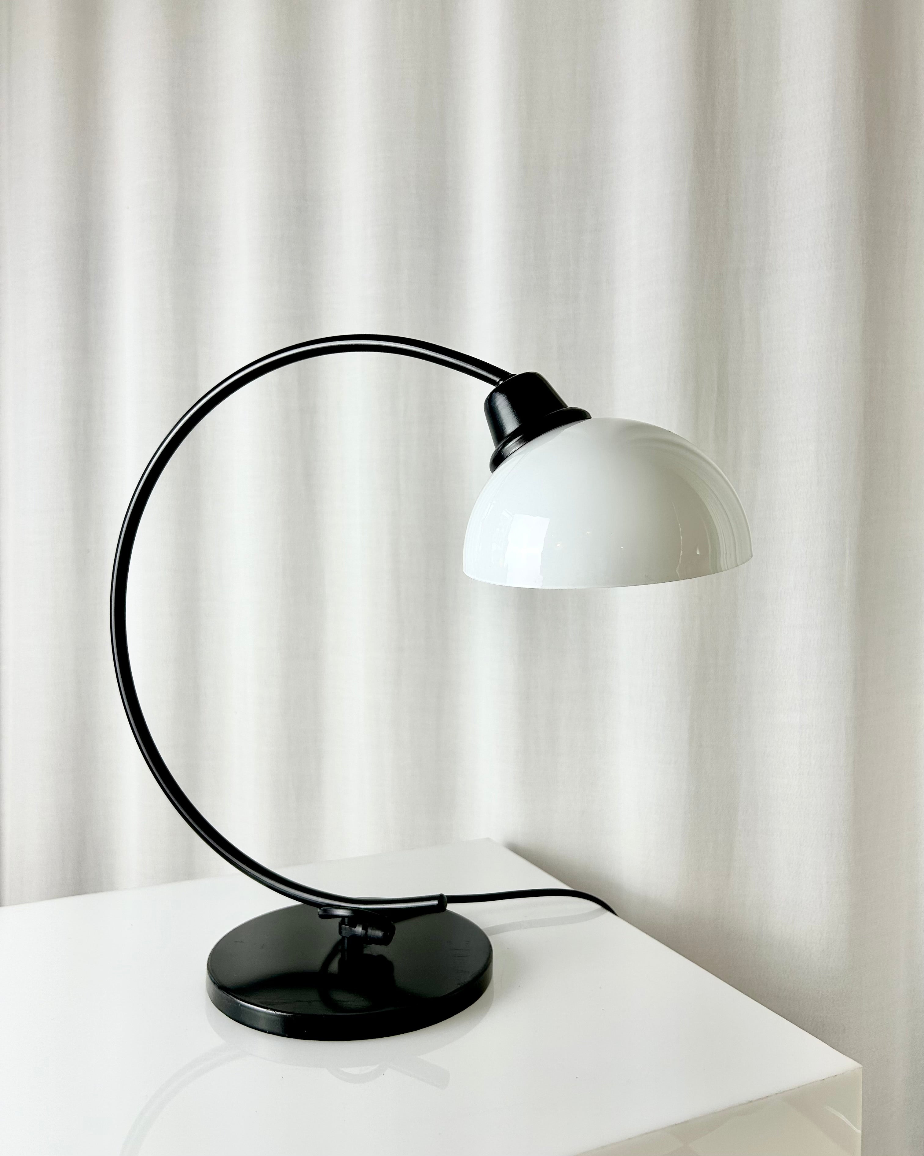 Vintage IKEA Harmoni table lamp featuring a black arched metal frame and a white glass shade, 1980s postmodern design.