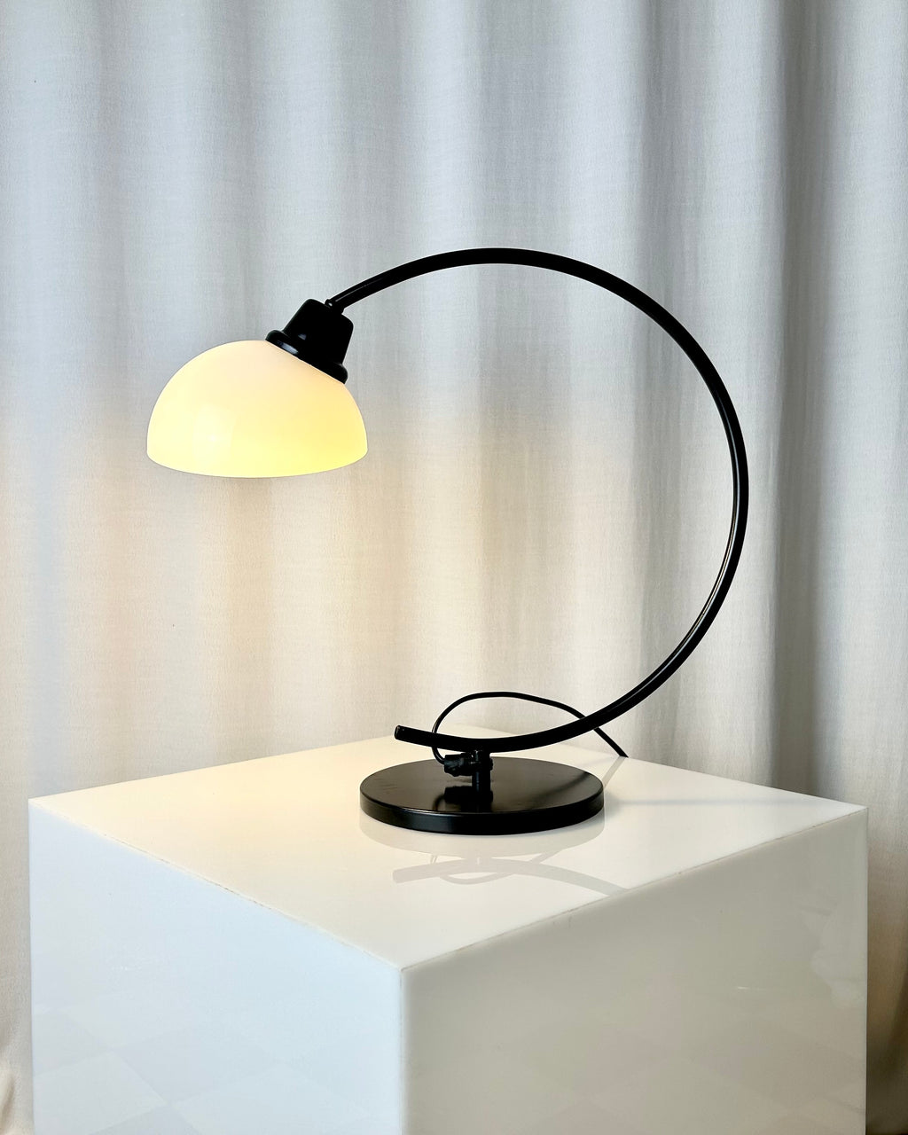 Vintage IKEA Harmoni table lamp featuring a black arched metal frame and a white glass shade, 1980s postmodern design.